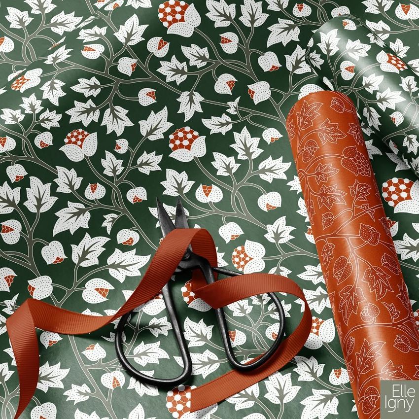 Gift wrapping paper mockup featuring a green sheet with white and red botanical patterns, scissors, ribbon, and a brown roll.