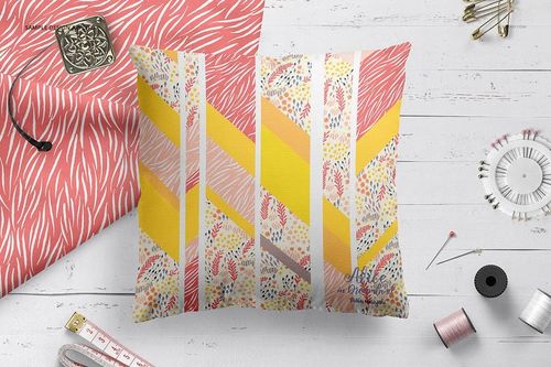 Mockup of a square pillow with colorful chevron and floral design, surrounded by sewing tools on a white table.