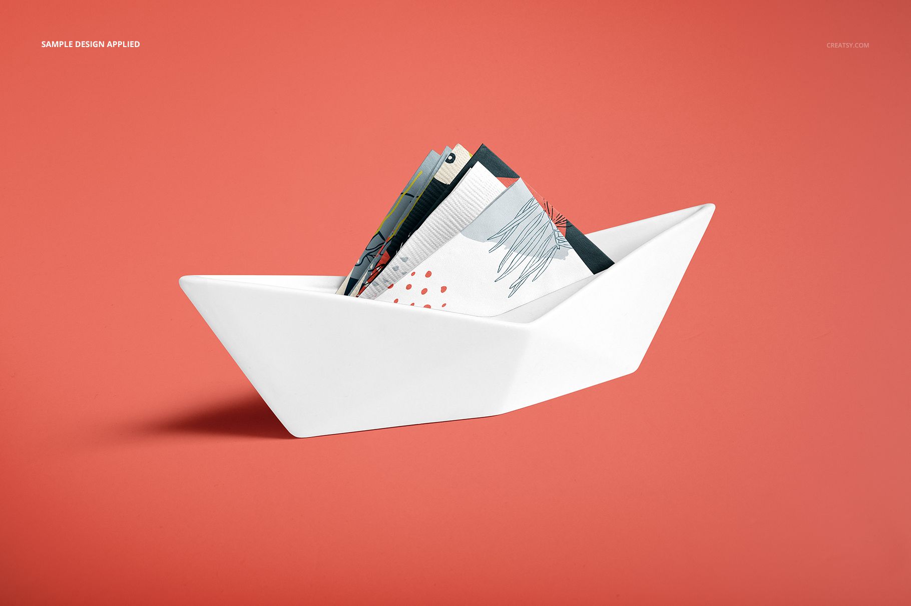 PSD mockup featuring paper napkins with graphic designs in a sleek white holder, viewed from the front on a coral surface.