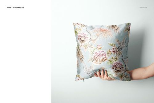 PSD mockup of a square pillow with a botanical design, shown being held horizontally in front of a minimalist wall.