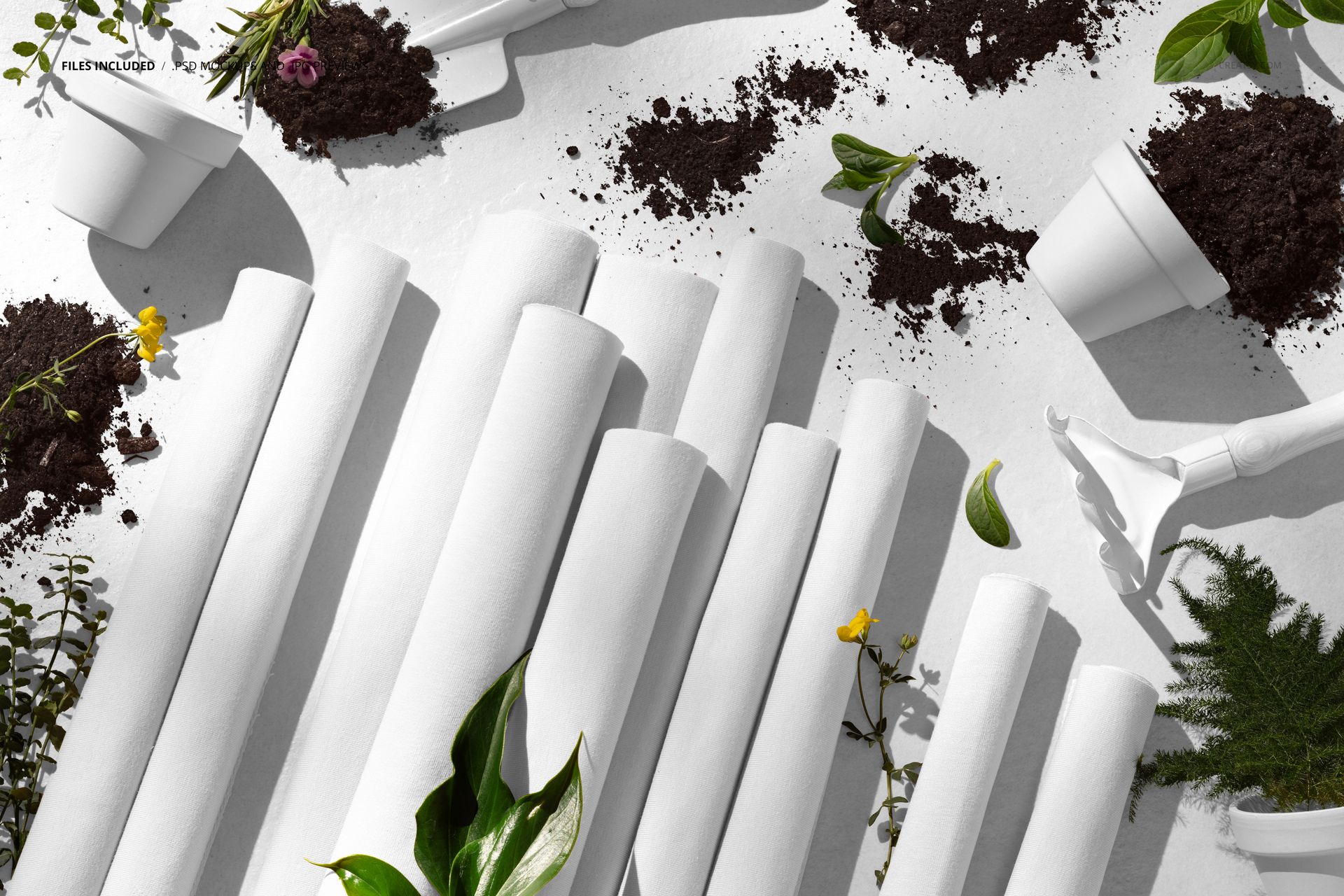 PSD mockup showing several white fabric rolls with garden tools, potted plants, and loose soil in a top-down view.