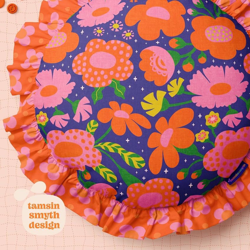 Ruffled pillow mockup featuring a bold floral pattern in orange, pink, and green on a dark blue background, viewed from above.