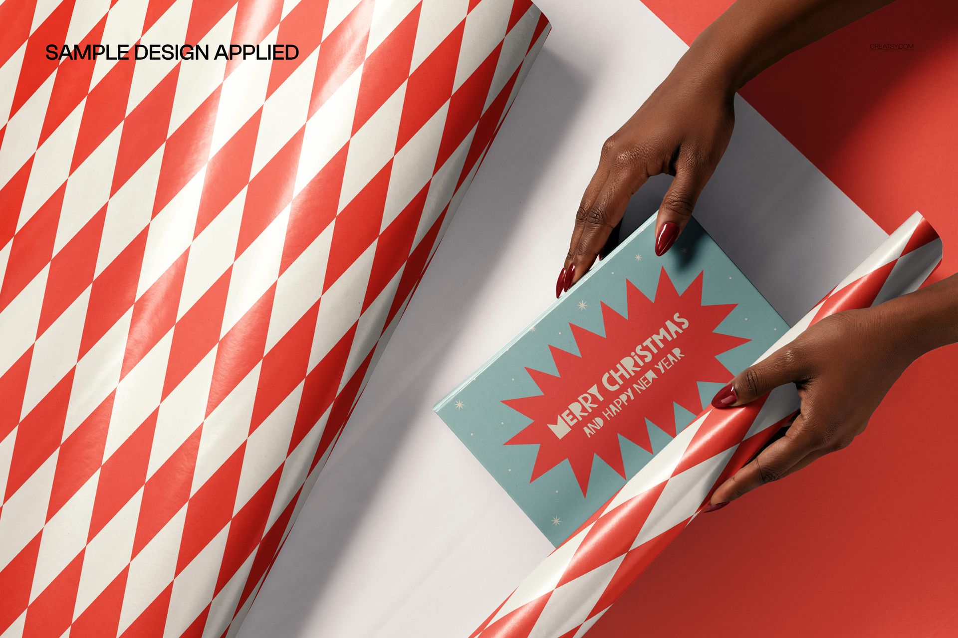 PSD mockup showing hands wrapping a box in red and white patterned paper, with a Christmas card on a red background.