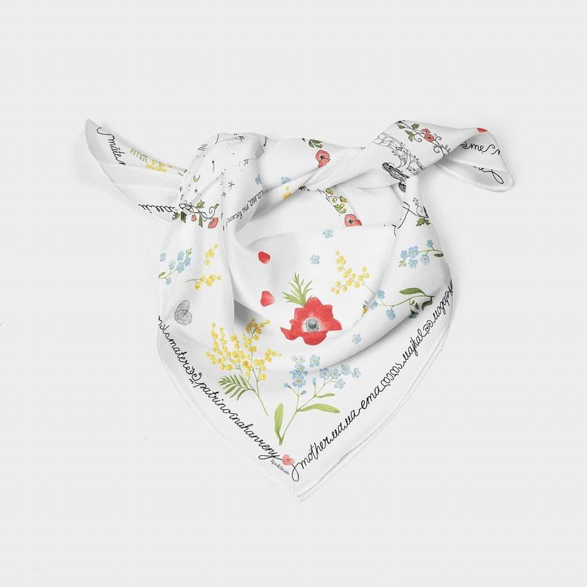 Silk scarf mockup featuring a white scarf with colorful floral patterns and handwritten-style text along the edge, displayed on a light background.