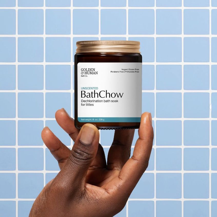 Hand holding a clear jar candle mockup with a white label against a blue tiled background, label features black and gold text.