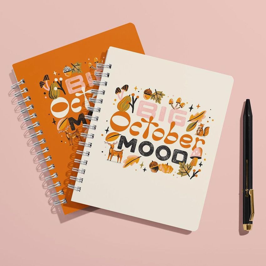 Two coiled notebook mockups with illustrated covers, one orange and one white, on a light pink background with a black pen.