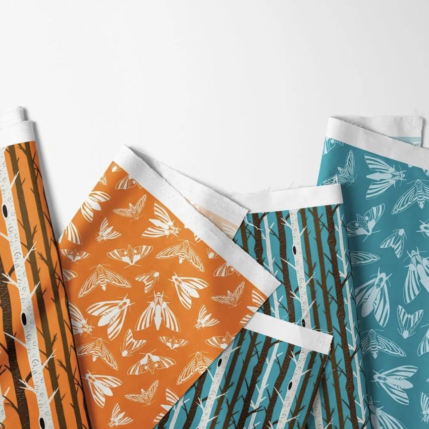 Folded fabrics mockup showing four fabric pieces with orange and teal backgrounds, featuring moth and branch patterns.