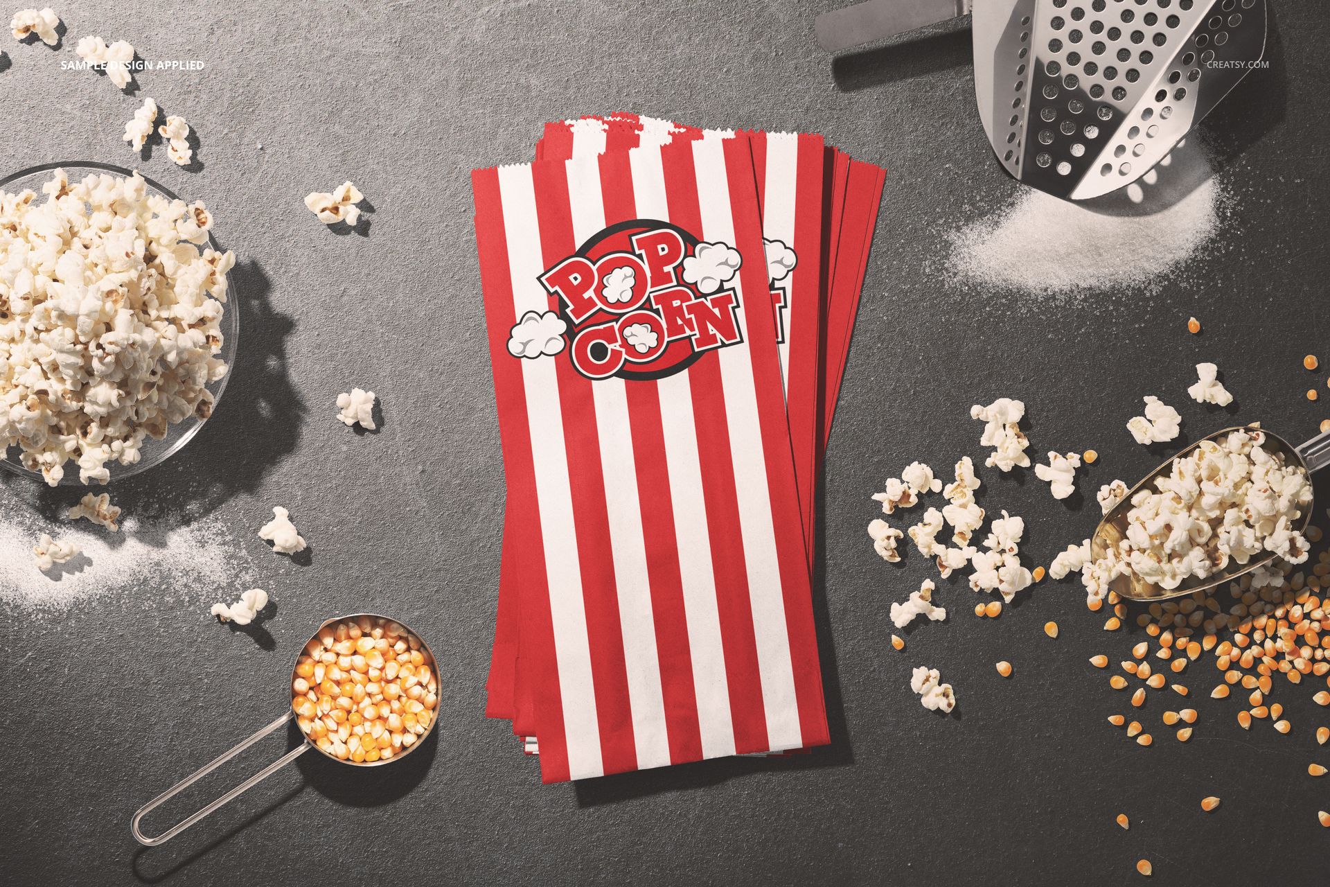 Popcorn paper bag PSD mockup featuring striped bags, loose popcorn, kernels, and kitchen props on a dark tabletop.