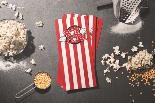 Popcorn paper bag PSD mockup featuring striped bags, loose popcorn, kernels, and kitchen props on a dark tabletop.