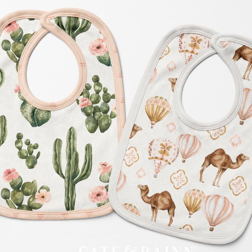 Two baby bibs mockup displayed on a white surface, one with a cactus and floral pattern, the other with camels and hot air balloons.