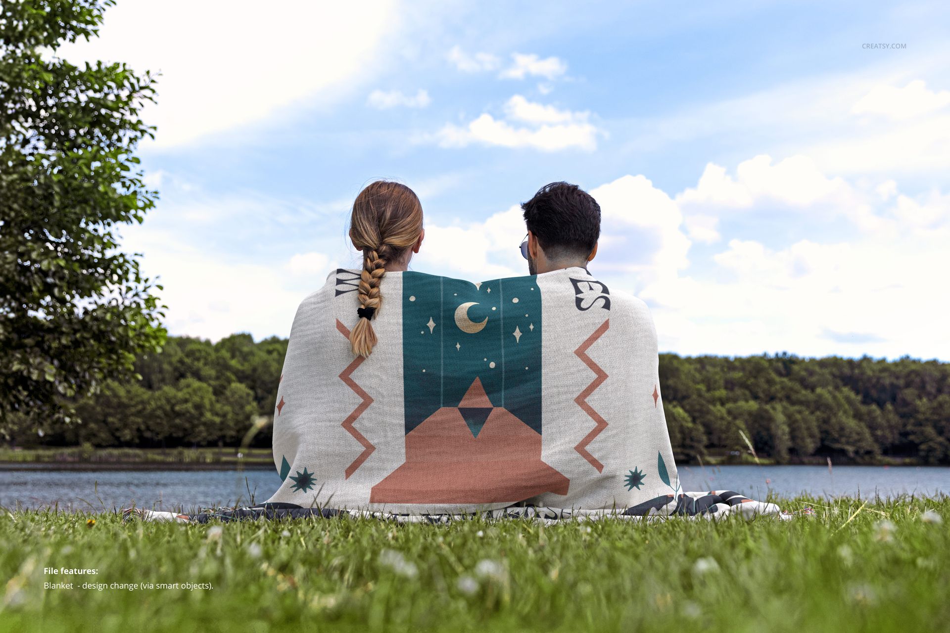 Jacquard throw blanket mockup draped around two people, with nature scenery and a forested lake in the background.