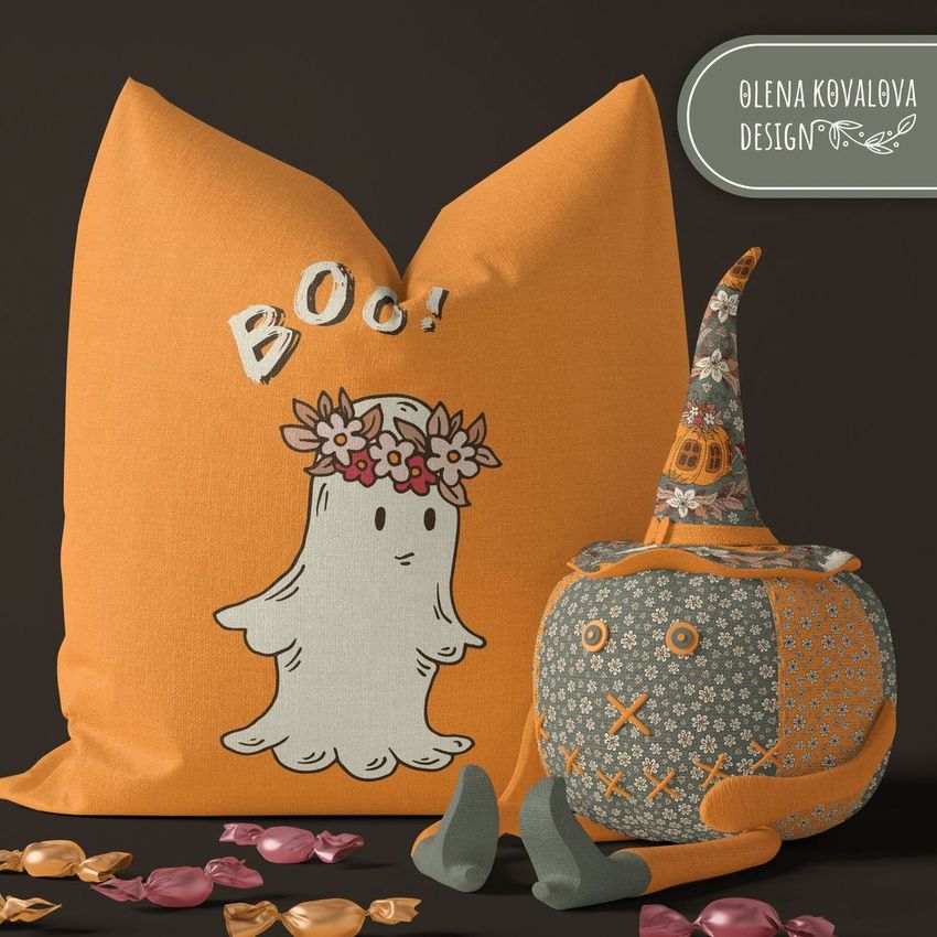 Halloween pillow mockup featuring an orange pillow with a cute ghost and 'Boo!' text, next to a toy pumpkin with a witch hat. Assorted candies are scattered on a dark surface.