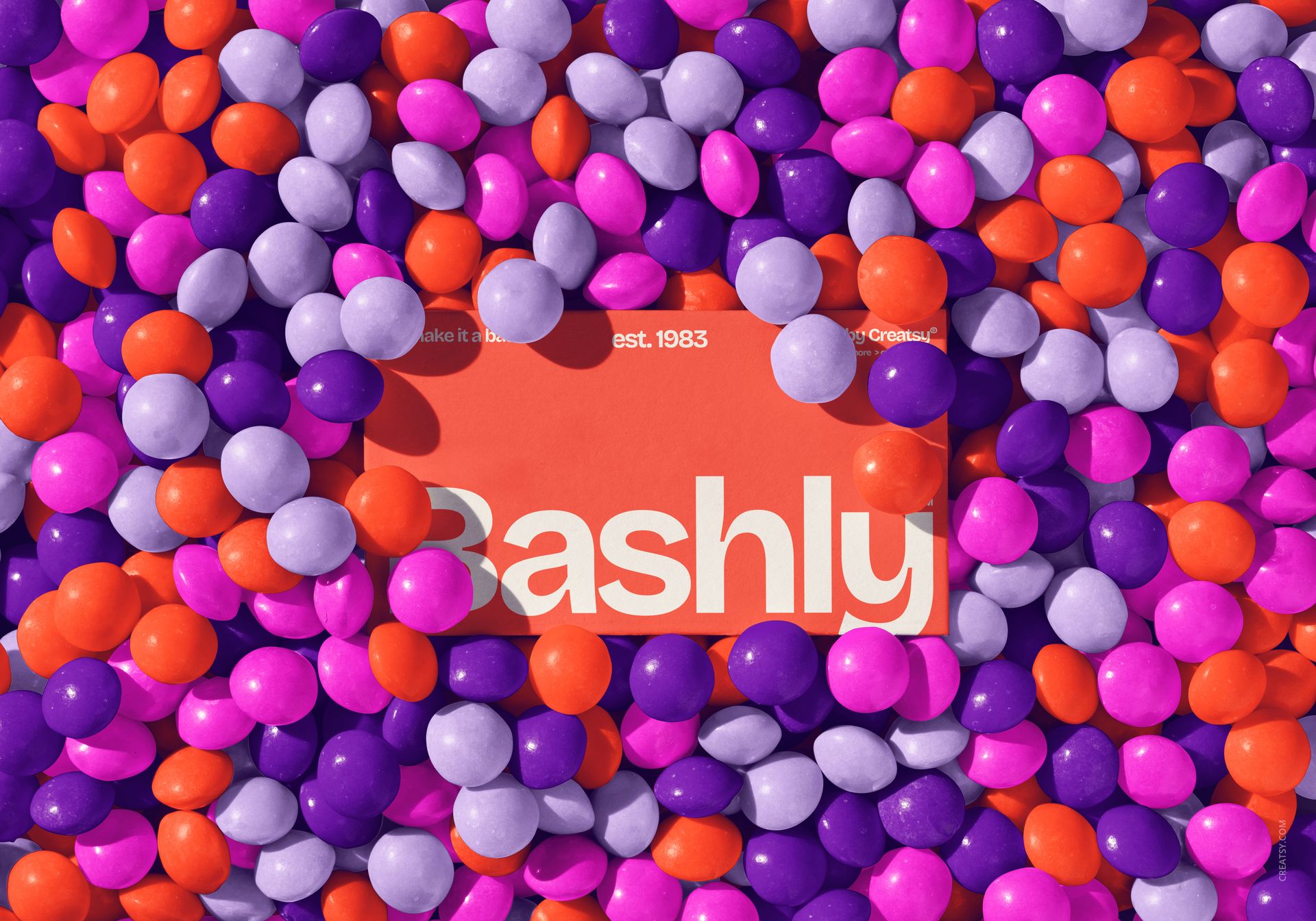 Rectangular orange card with bold white Bashly text surrounded by scattered orange, purple, and lavender party balls.