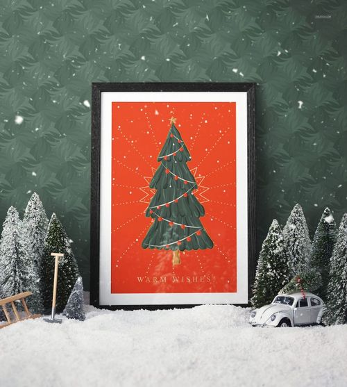 Framed Christmas tree illustration with warm wishes text, set against a red background, surrounded by snowy trees.