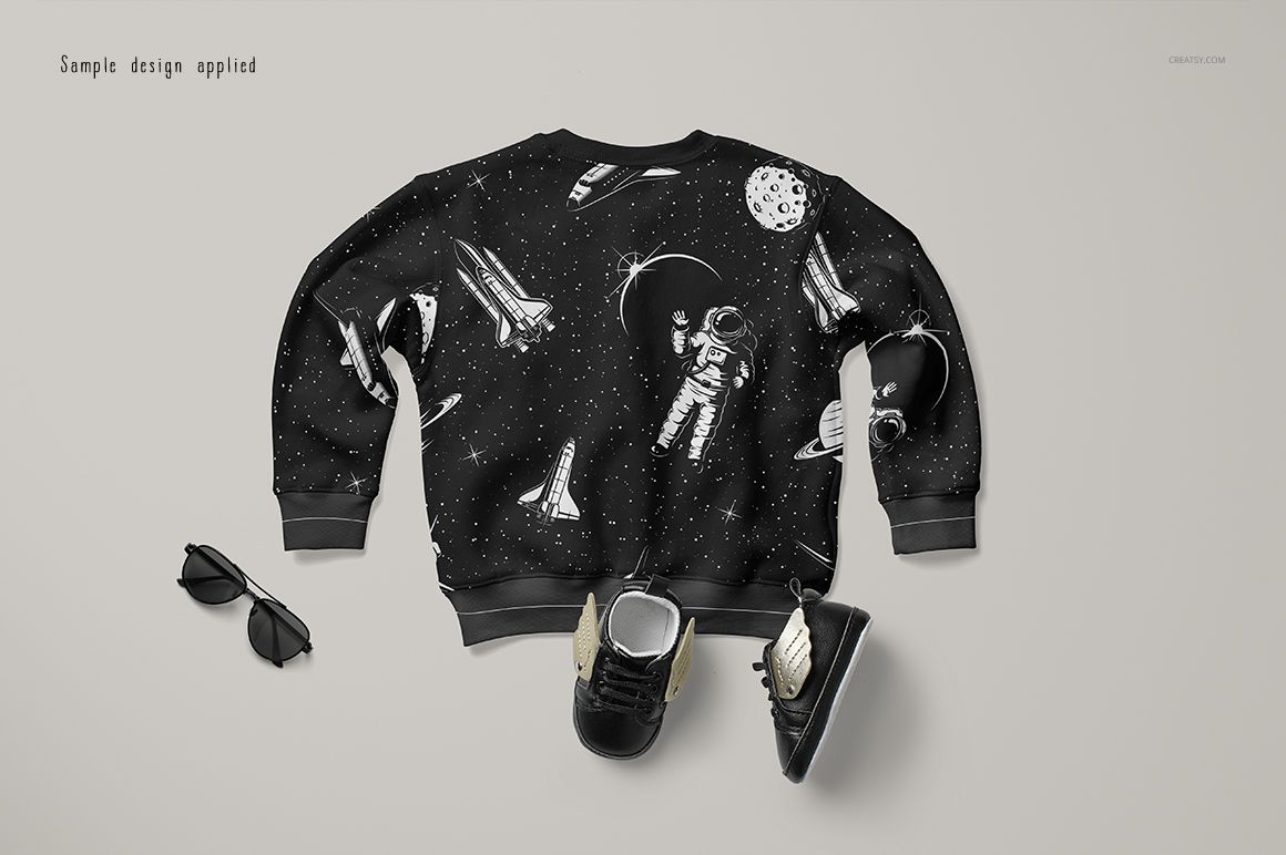 Baby sweatshirt mockup with black fabric featuring white space-themed illustrations, shown from the back on a light surface.