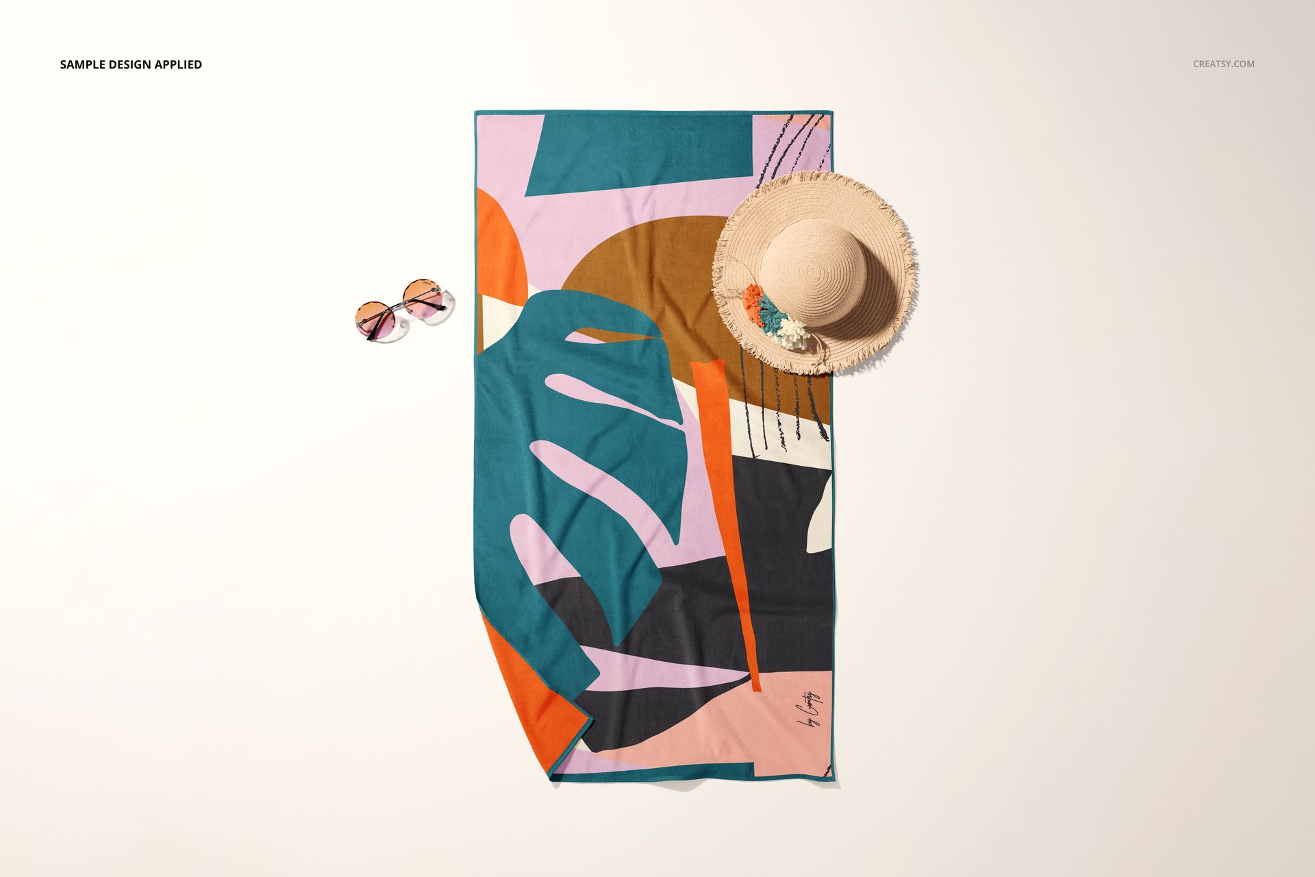Top view of a beach towel mockup featuring bold geometric shapes, styled with sunglasses and a straw hat beside it.