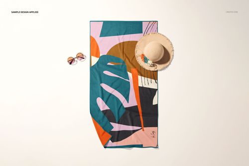 Top view of a beach towel mockup featuring bold geometric shapes, styled with sunglasses and a straw hat beside it.