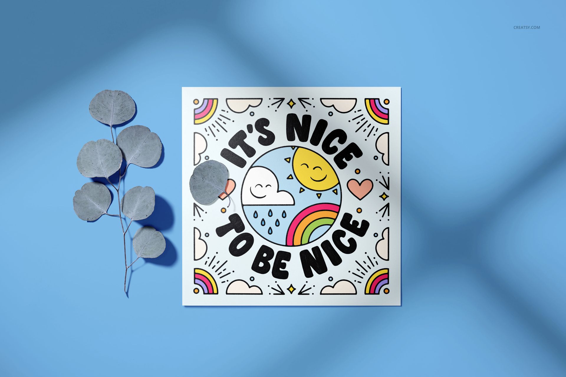 PSD mockup of a square stationery card with cheerful clouds, sun, and rainbow designs, next to dried leaves on blue.