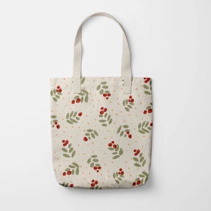Polyester tote bag mockup featuring a cream-colored bag with a scattered berry and leaf pattern, shown on a plain white background.