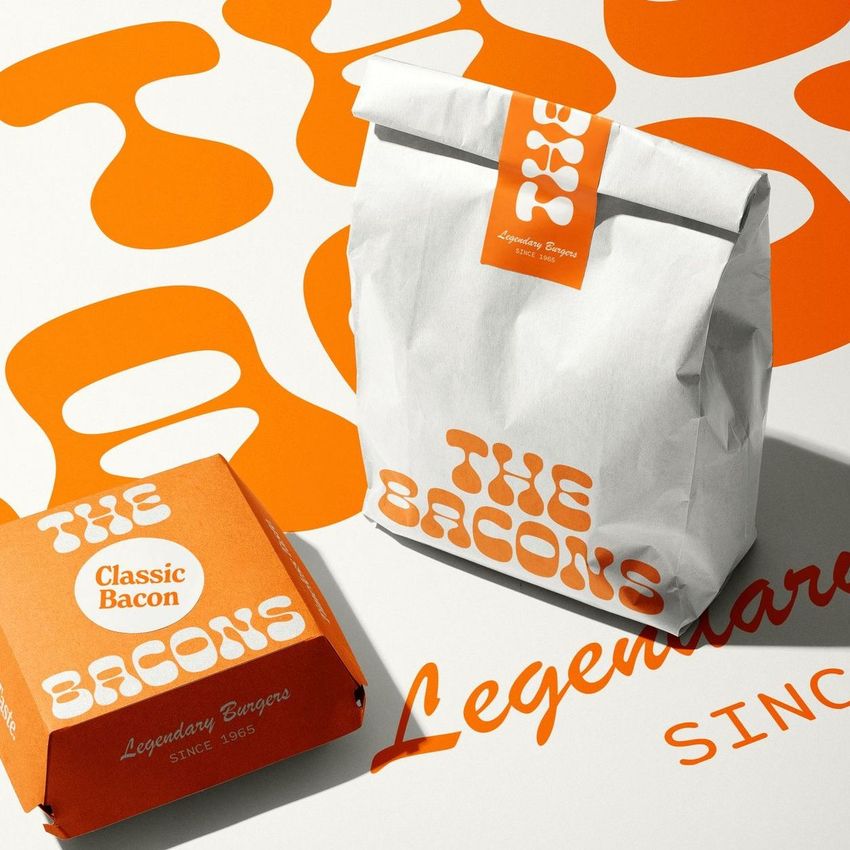 Burger packaging mockup featuring a paper bag, burger box, and printed menu with bold orange and white retro patterns and text.
