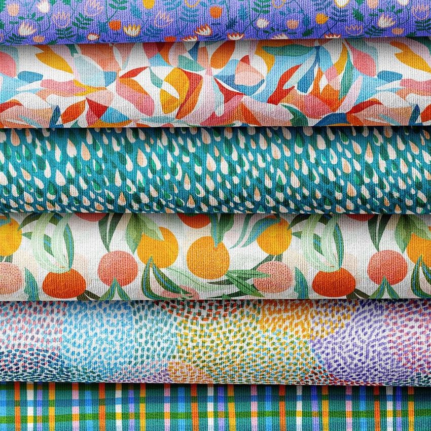 Fabric stack mockup showing six folded textiles with colorful patterns, including florals, abstract shapes, and fruit motifs.