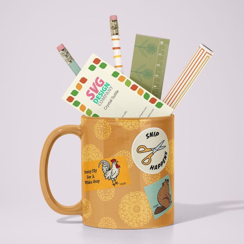 Mug mockup with a tan floral pattern, decorated with stickers, holding pencils, a ruler, and business cards on a light background.