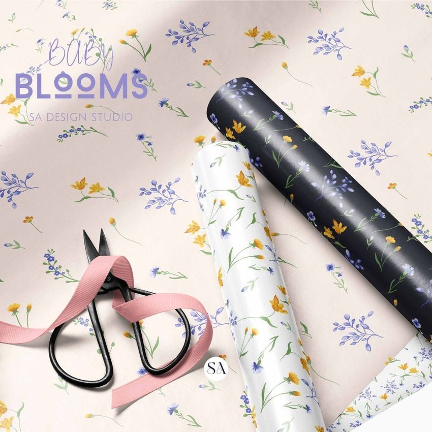 Gift wrapping paper mockup showing three floral patterned rolls on a light surface, with scissors and a pink ribbon nearby.