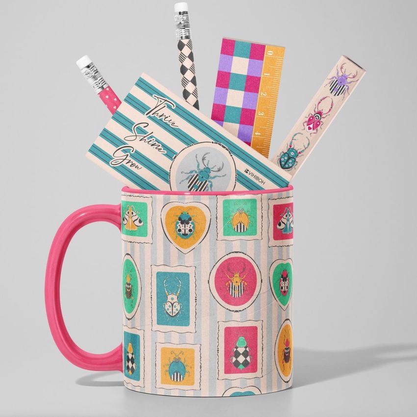 Mug mockup with a pink handle, decorated with colorful bug illustrations, holding pencils, a ruler, and stationery on a gray background.