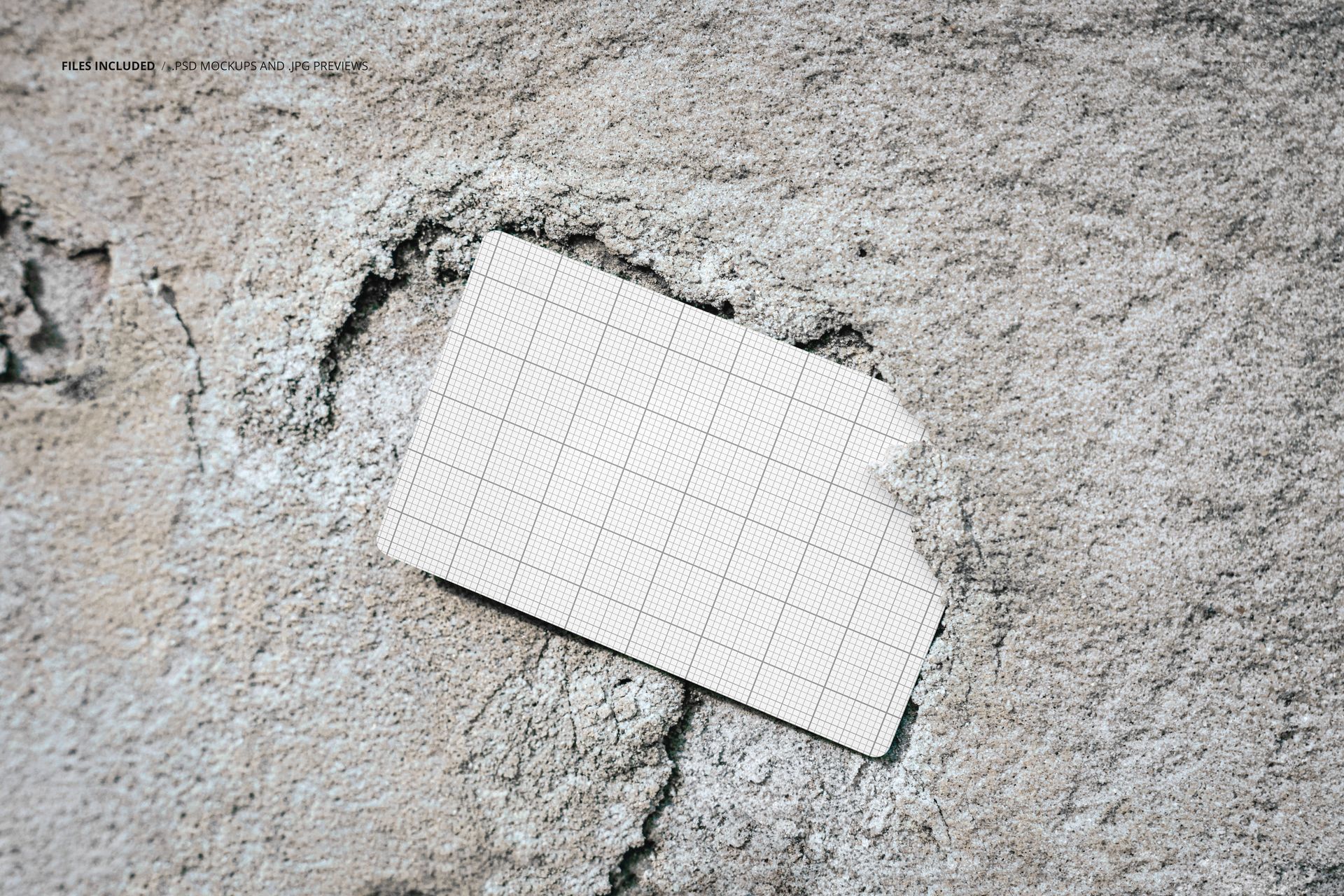 Grid-patterned business card mockup stuck in a cracked, light gray wall, shown from a top-down perspective.