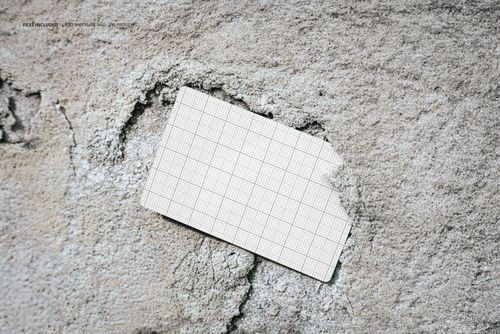 Grid-patterned business card mockup stuck in a cracked, light gray wall, shown from a top-down perspective.