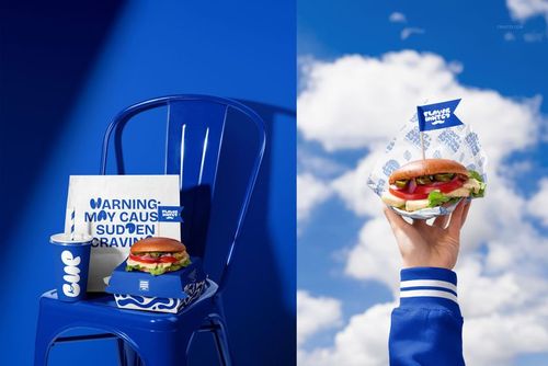 Vegan burger packaging mockup featuring a burger, drink cup, and branded box on a blue metal chair with a vivid blue background.