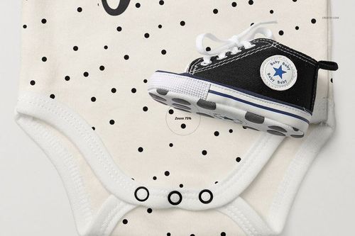 Front view of a baby longsleeve onesie mockup with black polka dot pattern, shown with a black baby sneaker on top.