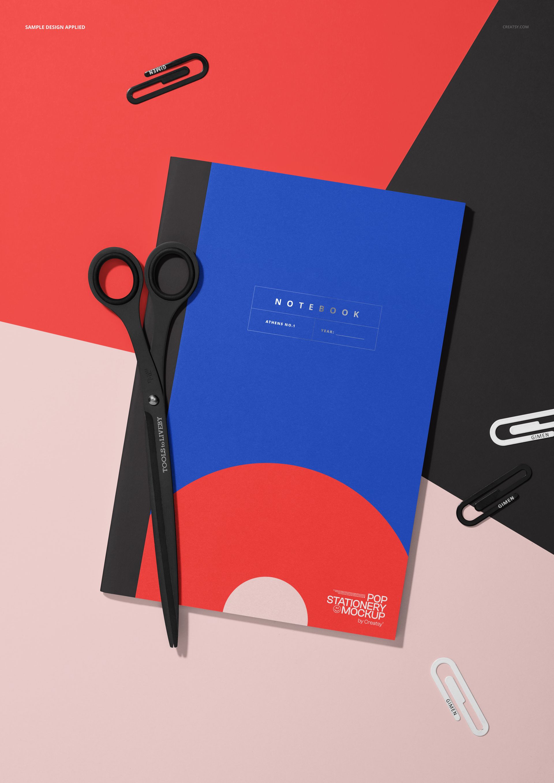 Classic notebook mockup with scissors and paper clips on a geometric red, black, and pink surface, top view.
