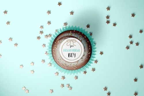 PSD mockup showing a cupcake with blue paper wrap and custom topper, placed amid metallic star-shaped confetti.