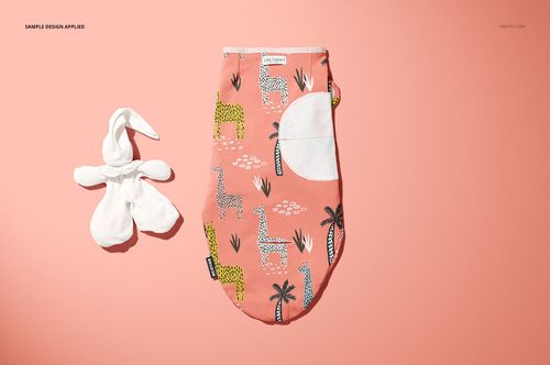 Top view of a baby swaddle wrap mockup featuring a coral color, giraffe and palm tree print, and a soft white toy beside it.