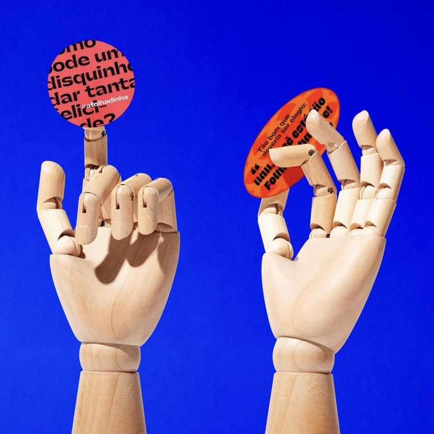 Sticker mockup featuring two wooden mannequin hands holding round and oval stickers with bold text on a solid blue background.