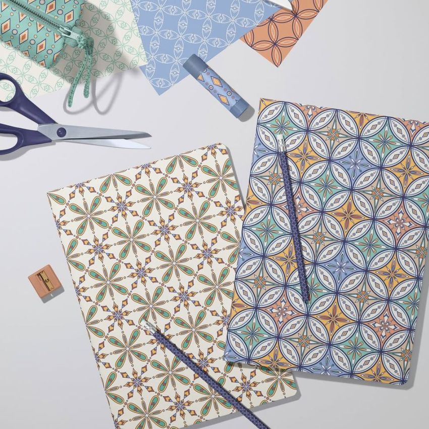 Stationery mockup featuring two classic A4 notebooks with geometric kaleidoscope patterns, pencils, and scissors on a light surface.