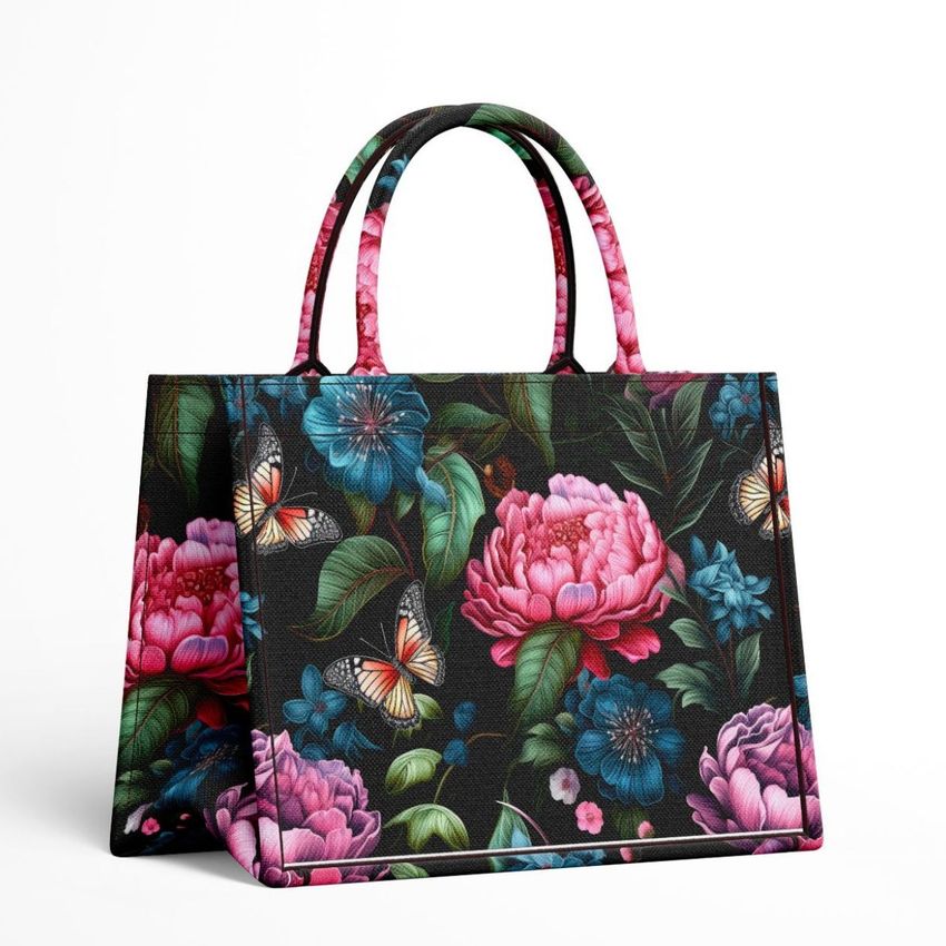 Canvas tote bag mockup featuring a dark background with vibrant floral and butterfly patterns, photographed on a white surface.