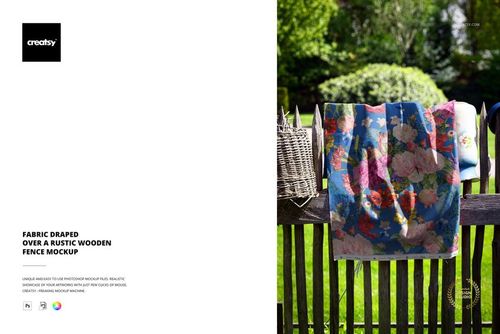 PSD mockup showing a vibrant fabric with a flower design hanging over a weathered fence, surrounded by greenery.