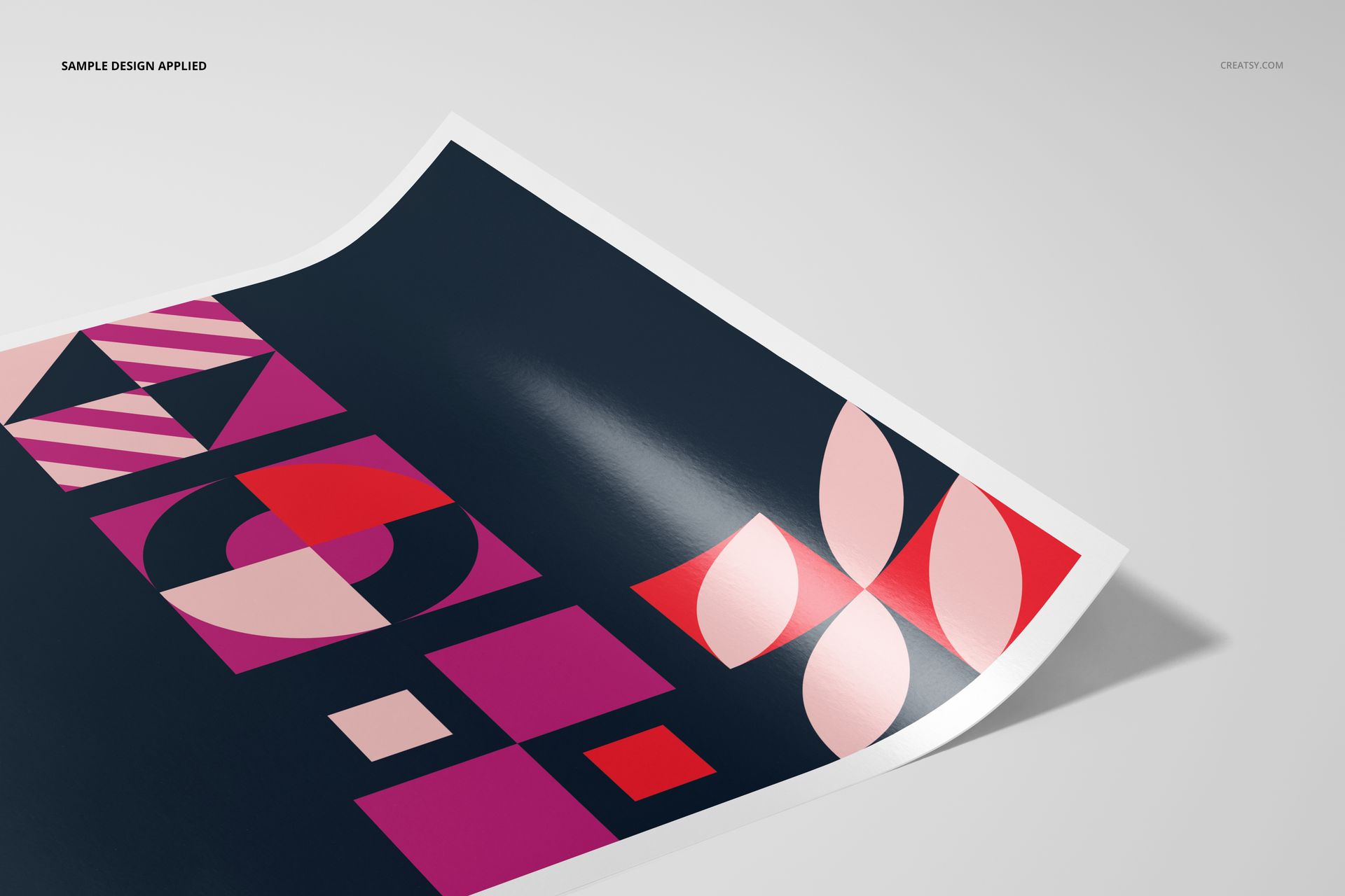 Glossy fine art print mockup featuring geometric shapes in pink and red on a dark background, shown from a corner angle.