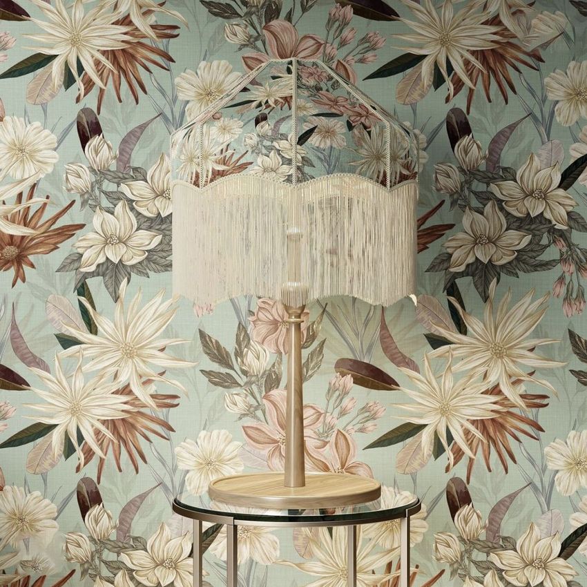 Tassel shade table lamp mockup on a round glass table, set against a floral wallpaper with beige and brown tones.