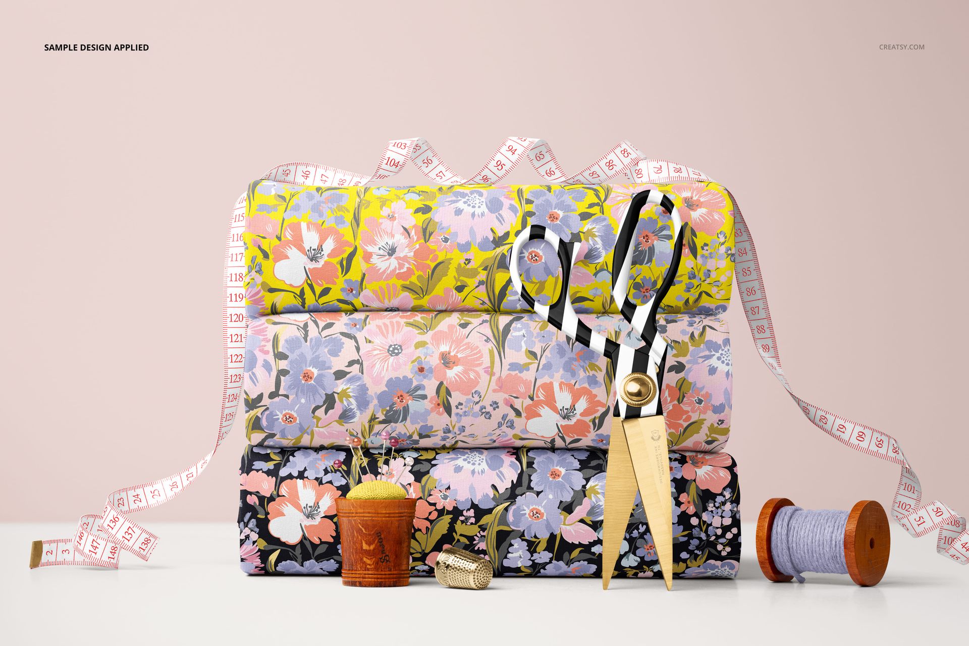 PSD mockup displaying layered floral jersey fabrics, scissors, thimble, and tape measure on a light pink background.
