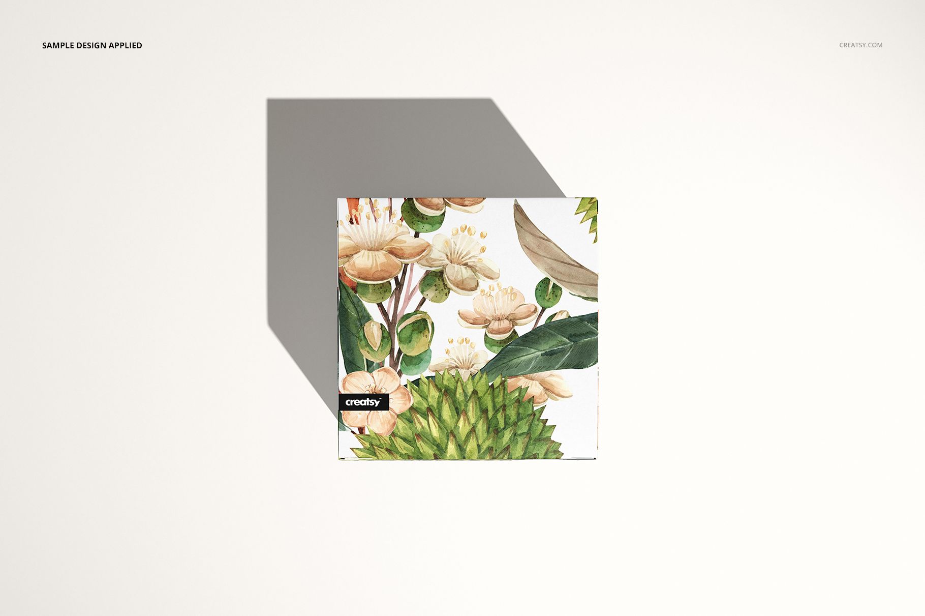 Square candle packaging mockup featuring green and beige floral artwork, shown from above on a neutral surface.