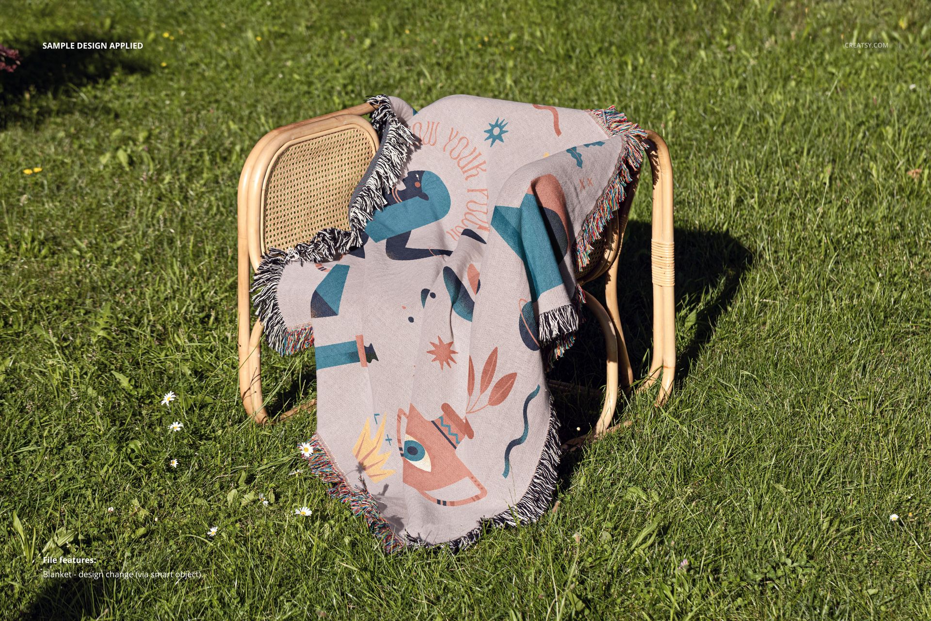 Jacquard fringed throw blanket mockup featuring playful shapes and colors, displayed on a chair in a grassy yard.