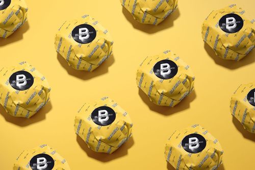 Burgers wrapped in yellow patterned paper mockup, each featuring a black circular label, shown from a top angle.