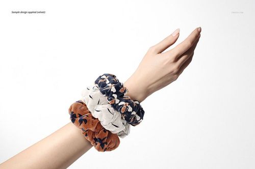PSD mockup showing a hand with assorted fabric hair scrunchies in orange, cream, and dark blue floral designs.