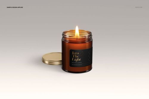 Front view of an amber jar candle mockup with a burning wick, gold lid off to the side, and a dark label design.
