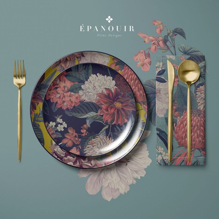 Placemat napkin plate mockup showing a floral plate, matching napkin, and gold cutlery on a blue surface with flower designs.