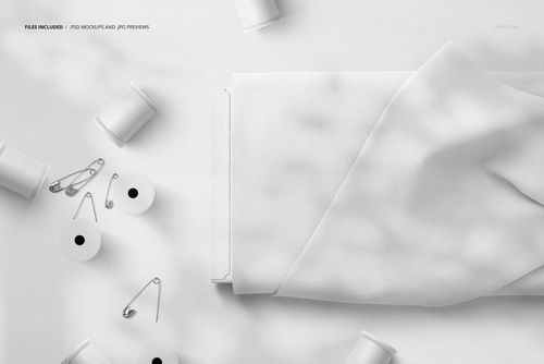 Thread spools and safety pins scattered near a folded fabric bolt with draped white cloth, shown from above in a PSD mockup.