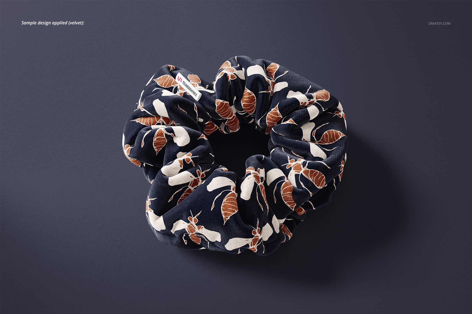 Mockup of a fabric hair scrunchie featuring a botanical print in white and brown, displayed from above on a solid surface.